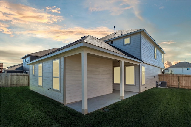 back house at dusk featuring a patio area, a yard, and central AC unit