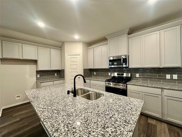 kitchen featuring light stone countertops, stainless steel appliances, a center island with sink, and sink