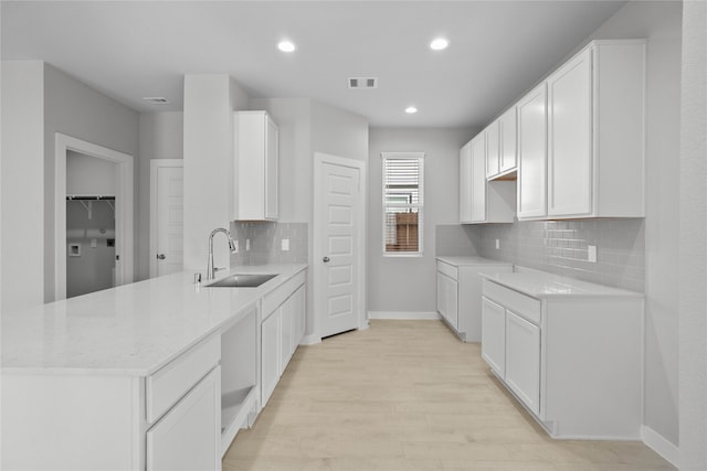 kitchen featuring white cabinets, backsplash, light wood-type flooring, and sink