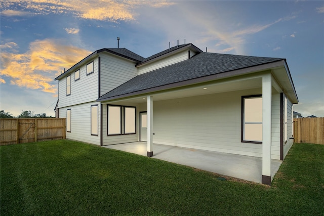 back house at dusk with a lawn and a patio area