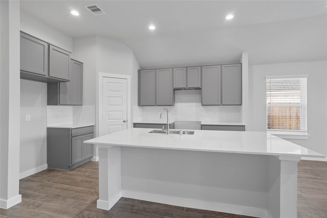 kitchen with gray cabinetry, sink, dark hardwood / wood-style flooring, an island with sink, and lofted ceiling