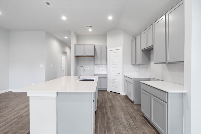 kitchen featuring sink, dark hardwood / wood-style floors, an island with sink, gray cabinets, and decorative backsplash