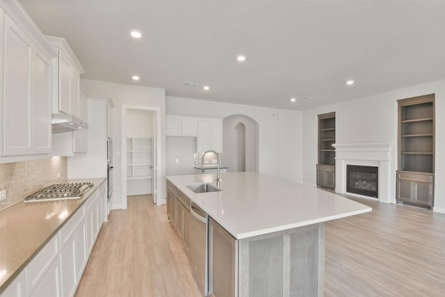 kitchen with a large island with sink, white cabinets, sink, light hardwood / wood-style floors, and stainless steel appliances