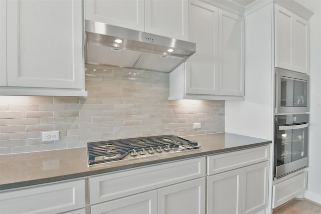 kitchen with ventilation hood, white cabinets, decorative backsplash, light wood-type flooring, and stainless steel appliances