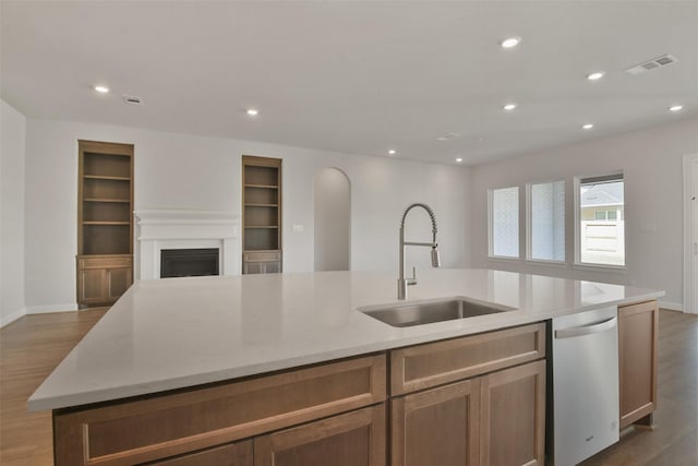 kitchen with stainless steel dishwasher, sink, a kitchen island with sink, and dark wood-type flooring