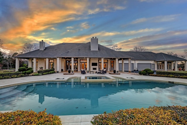 pool at dusk with a patio area and an in ground hot tub