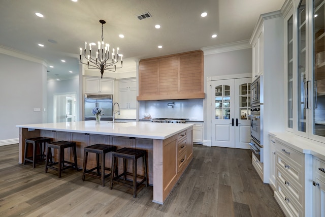 kitchen with a large island, dark hardwood / wood-style floors, built in appliances, crown molding, and white cabinets