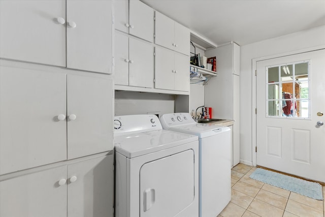 clothes washing area with cabinets, sink, light tile floors, and washing machine and clothes dryer