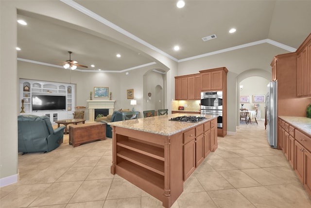 kitchen featuring appliances with stainless steel finishes, light stone counters, ornamental molding, ceiling fan, and a kitchen island