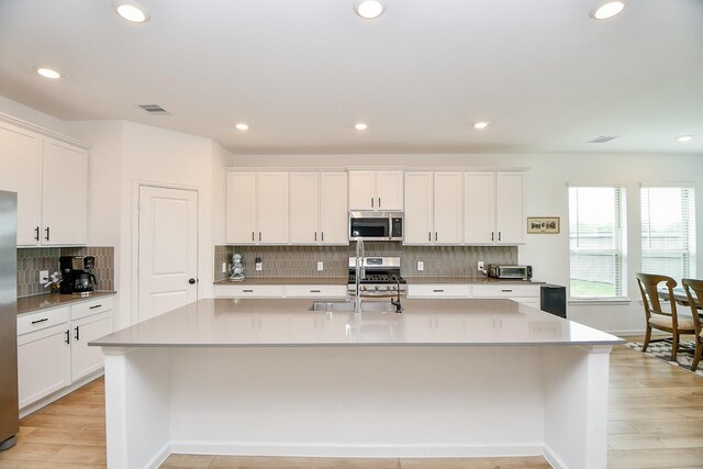 kitchen with tasteful backsplash, a center island with sink, light wood-type flooring, sink, and appliances with stainless steel finishes