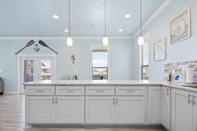 kitchen featuring white cabinetry, hanging light fixtures, light stone counters, crown molding, and light hardwood / wood-style floors