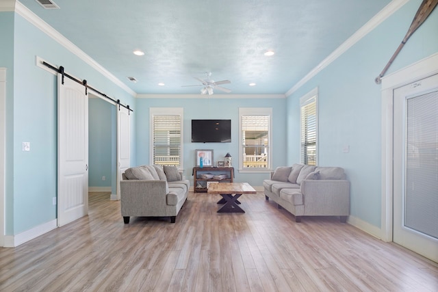 living room with a barn door, ceiling fan, light hardwood / wood-style flooring, and ornamental molding