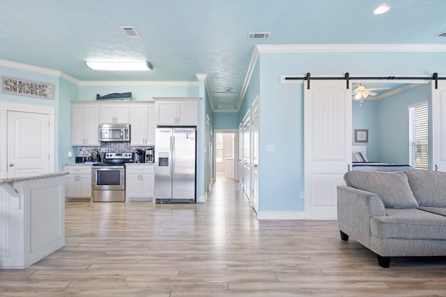 kitchen with a barn door, crown molding, white cabinets, and appliances with stainless steel finishes