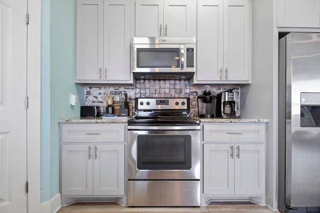 kitchen with white cabinets, decorative backsplash, light stone countertops, and appliances with stainless steel finishes