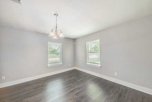 spare room with a wealth of natural light, dark hardwood / wood-style flooring, and an inviting chandelier