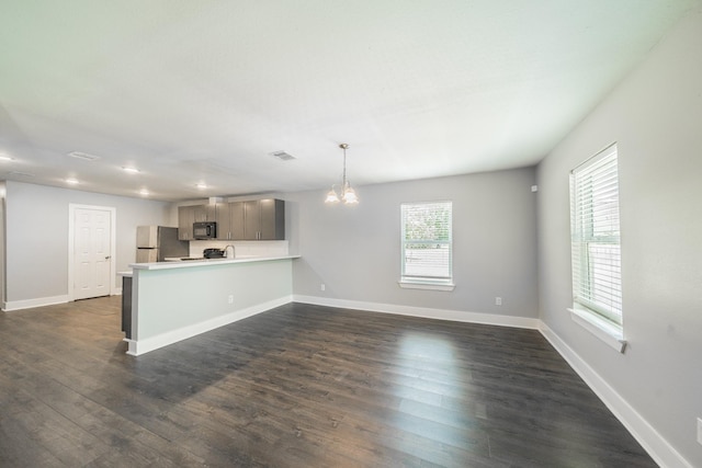 kitchen featuring stainless steel refrigerator, hanging light fixtures, dark hardwood / wood-style floors, a notable chandelier, and kitchen peninsula