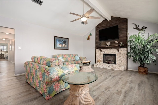 living room with a stone fireplace, ceiling fan, vaulted ceiling with beams, and hardwood / wood-style floors