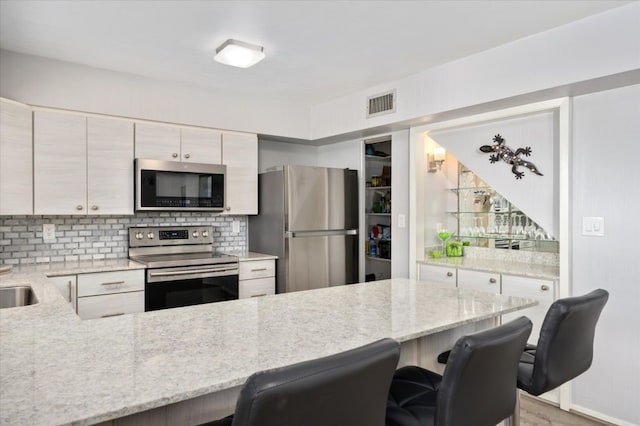 kitchen with light stone countertops, backsplash, a breakfast bar area, and stainless steel appliances