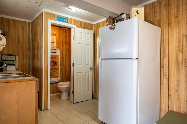 kitchen featuring ornamental molding, white fridge, wooden walls, and light tile floors