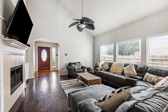 living room with ceiling fan, dark hardwood / wood-style floors, high vaulted ceiling, and a tiled fireplace