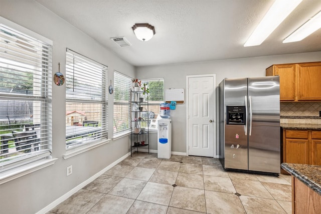 kitchen featuring backsplash, stainless steel fridge, plenty of natural light, dark stone counters, and light tile patterned flooring