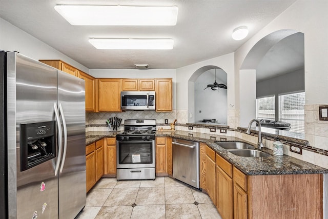 kitchen featuring dark stone counters, sink, light tile patterned floors, appliances with stainless steel finishes, and kitchen peninsula