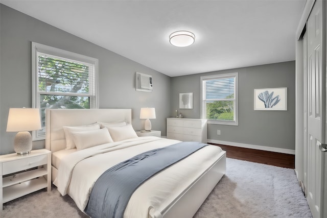 bedroom with a wall mounted air conditioner, a closet, light hardwood / wood-style floors, and multiple windows