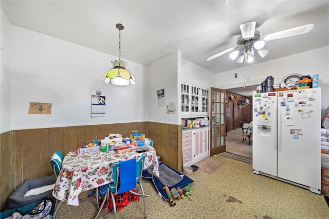 dining space with wooden walls, ceiling fan, and light colored carpet