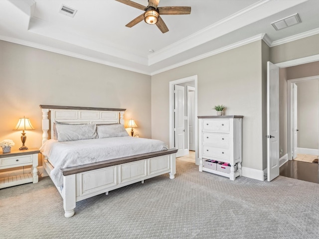 carpeted bedroom with a tray ceiling, baseboards, visible vents, and crown molding