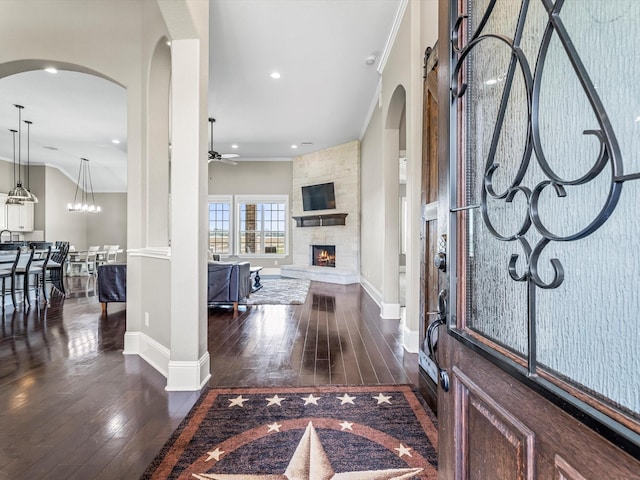 entrance foyer featuring baseboards, arched walkways, ceiling fan, dark wood-style flooring, and a fireplace