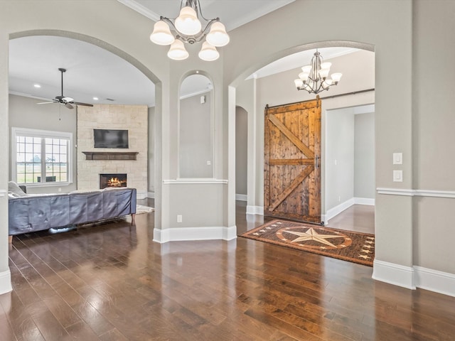 entryway featuring a stone fireplace, ceiling fan with notable chandelier, wood finished floors, baseboards, and ornamental molding