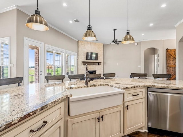 kitchen with arched walkways, a stone fireplace, a sink, stainless steel dishwasher, and crown molding