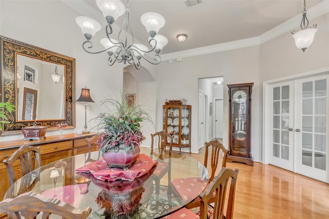 dining space featuring french doors, ornamental molding, a chandelier, and light hardwood / wood-style floors