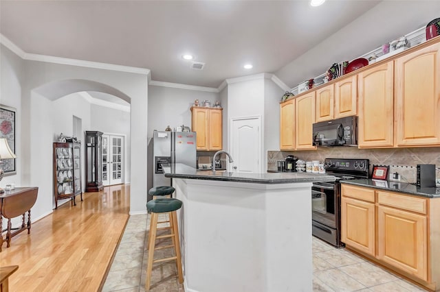 kitchen featuring tasteful backsplash, a kitchen island with sink, light brown cabinets, and black appliances