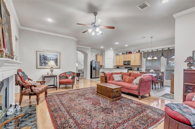 living room with crown molding, ceiling fan, a premium fireplace, and light hardwood / wood-style floors