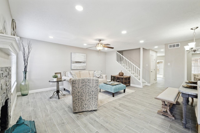 living room with a fireplace and ceiling fan with notable chandelier