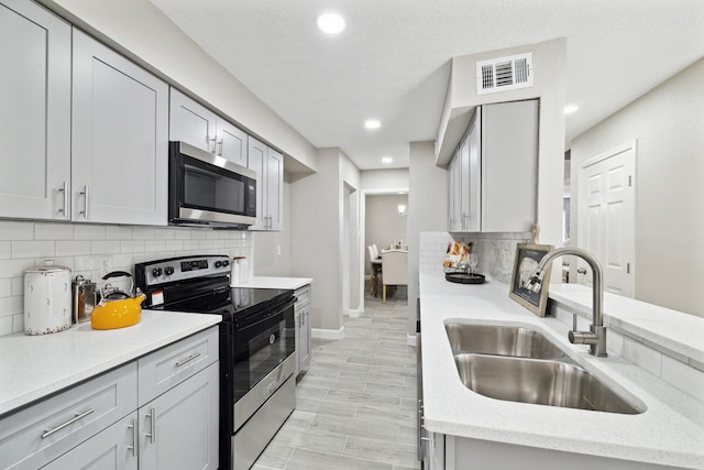 kitchen featuring decorative backsplash, appliances with stainless steel finishes, light stone counters, gray cabinetry, and sink