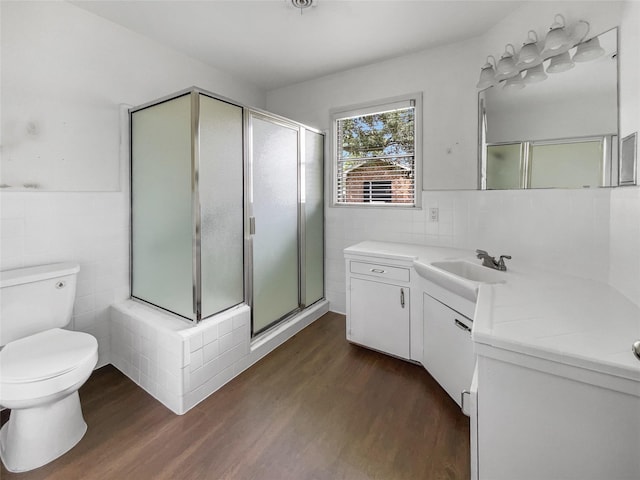 bathroom with toilet, a shower with shower door, hardwood / wood-style floors, tile walls, and vanity