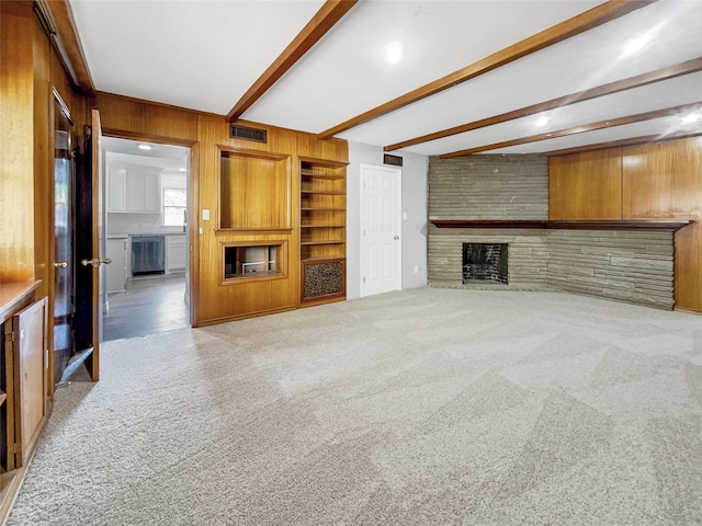 unfurnished living room with light carpet, beam ceiling, built in shelves, a large fireplace, and wooden walls