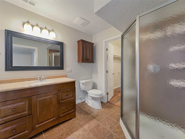 bathroom featuring toilet, tile floors, a shower with shower door, vanity, and a textured ceiling