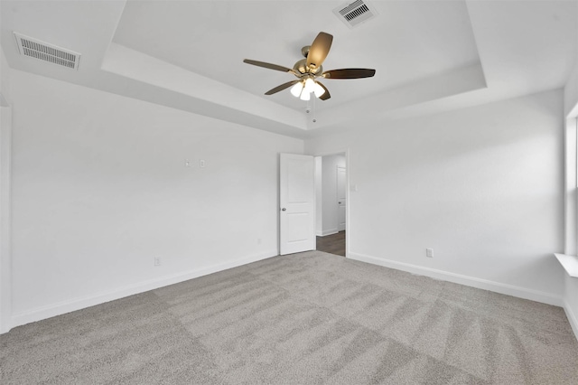 carpeted spare room with a raised ceiling and ceiling fan