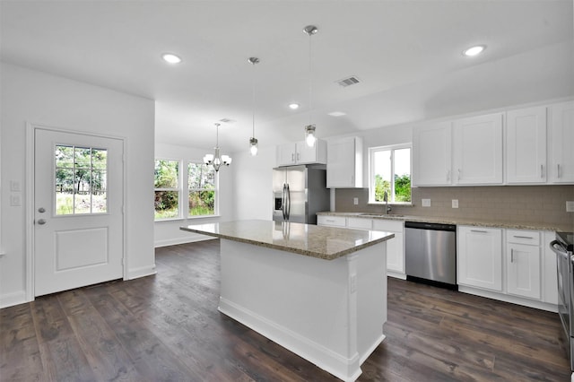 kitchen with dark wood-type flooring, hanging light fixtures, a kitchen island, white cabinetry, and stainless steel appliances