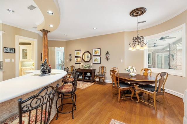 dining space with ornate columns, light hardwood / wood-style floors, ceiling fan with notable chandelier, and ornamental molding