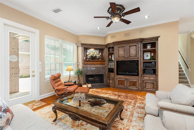 living room with a high end fireplace, light hardwood / wood-style floors, ceiling fan, and crown molding