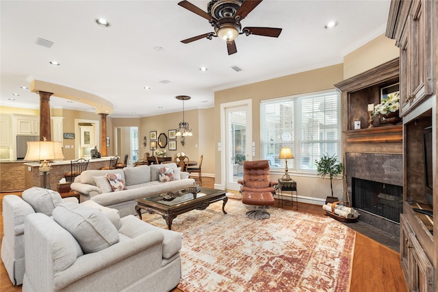 living room featuring ornate columns, ornamental molding, ceiling fan, wood-type flooring, and a premium fireplace