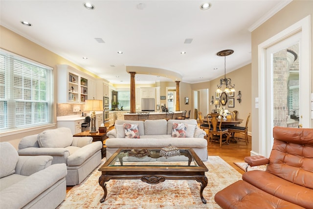 living room with ornate columns, light hardwood / wood-style flooring, a chandelier, and ornamental molding