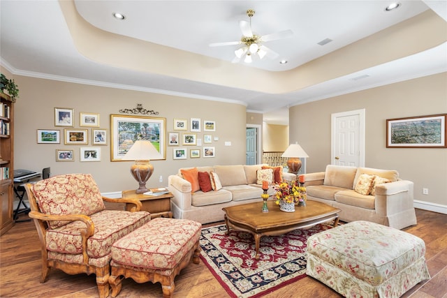 living room featuring hardwood / wood-style flooring, a raised ceiling, ceiling fan, and ornamental molding