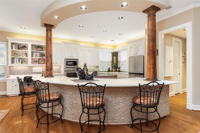 kitchen featuring white cabinetry, a kitchen bar, ornate columns, and stainless steel appliances