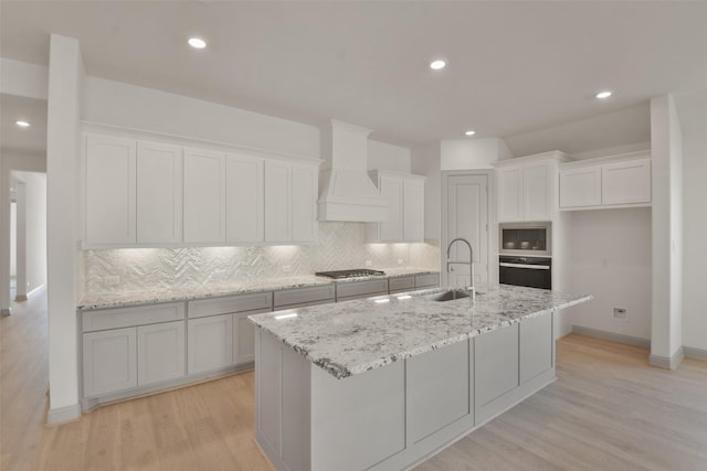 13318 Pine Lake Bnd, Tomball, TX 77375 - kitchen featuring light wood-type flooring, decorative backsplash, a center island with sink, custom exhaust hood, and appliances with stainless steel finishes