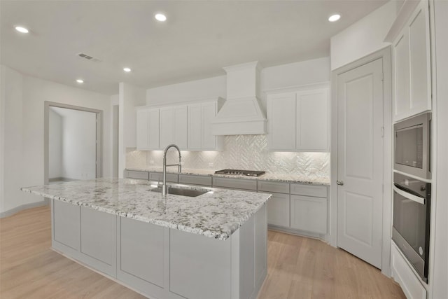 13318 Pine Lake Bnd, Tomball, TX 77375 - kitchen with sink, premium range hood, an island with sink, appliances with stainless steel finishes, and light wood-type flooring
